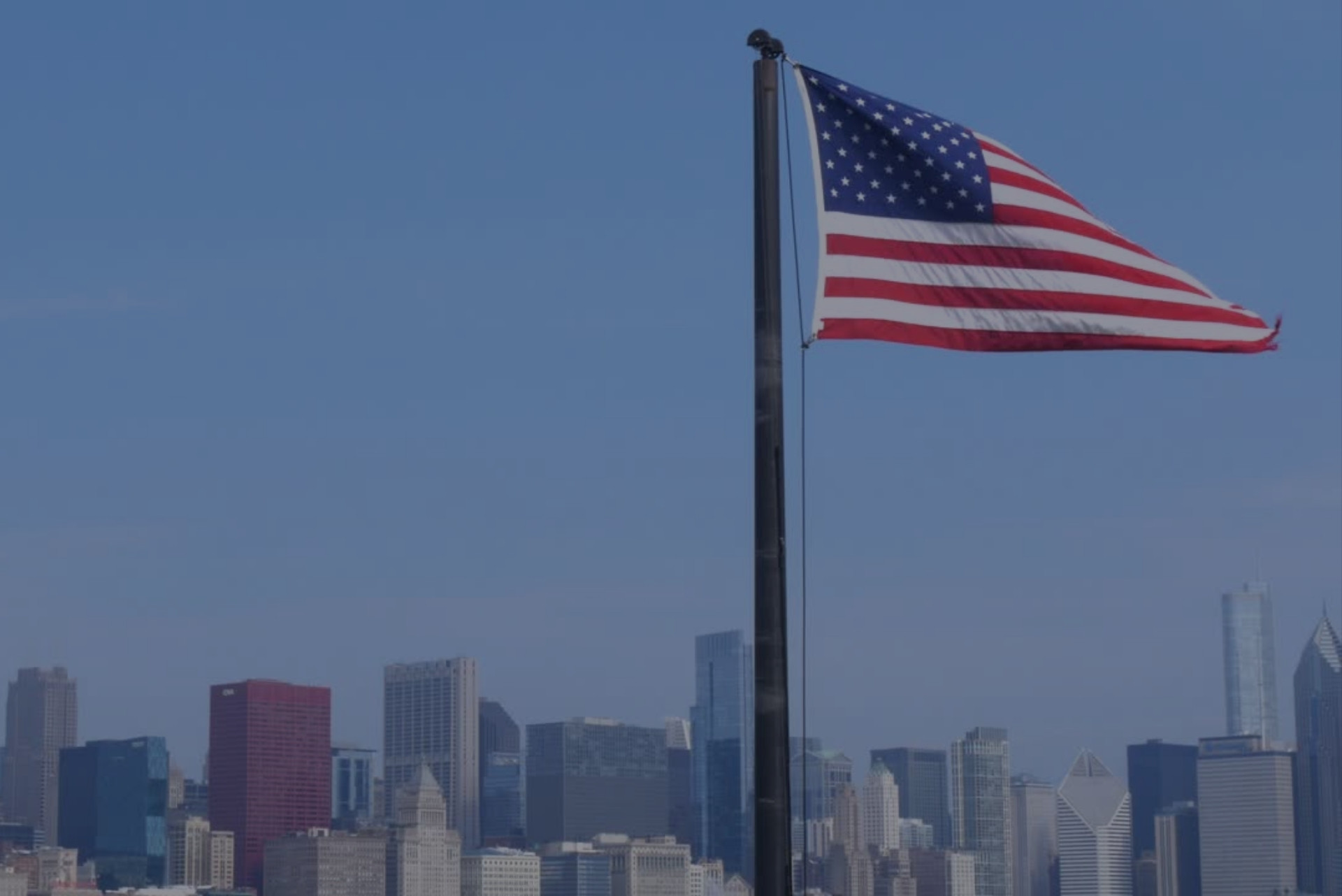 united states of america flag against a blue sky and the new york skyline